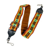 A vintage-style leather and woven fabric shoulder strap with a brown suede center, colorful geometric patterned webbing in orange, yellow, green, and black, and black leather hardware with silver metal clips on a white background.
