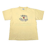 A pale yellow short-sleeve t-shirt with a graphic on the chest reading '100% MAMBO' in black outline letters around a red star, laid flat on a white background.