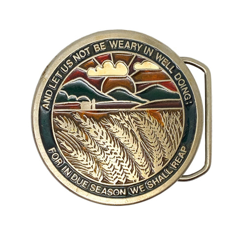 Metallic belt buckle with landscape design and text on a white background
