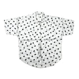 A white short-sleeve button-up shirt with an all-over black and gray abstract polka dot pattern, laid flat on a light gray fabric background.