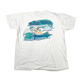 A white short-sleeve graphic t-shirt laid flat on a white surface, featuring a colorful retro-style print on the front with the text 'BAD DOG DOG DAY AFTERNOON' and a cartoon dog in a boat.