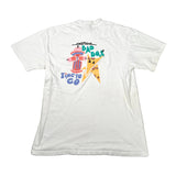 A white short-sleeve t-shirt laid flat on a light gray surface, showing a colorful graphic on the back. The graphic features a red fire hydrant, a yellow lightning bolt with black triangles, and stylized text reading 'AMERICAN BAD DOS' and 'TIME TO GO'.
