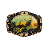 An oval-shaped vintage-style belt buckle featuring an embossed bull with antlers in a natural landscape, surrounded by an ornate antiqued bronze frame on a white background.