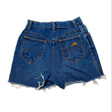 A pair of high-waisted blue denim shorts with a raw, frayed hem, shown from the back. The shorts feature two back pockets, with the right pocket decorated in gold embroidery reading 'Ru'.