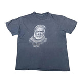A faded black short-sleeve t-shirt featuring a light gray graphic print of a portrait of King West (Emmanuel Kwame Nkrumah) with his name and birth/dead dates printed below, laid flat on a white background.
