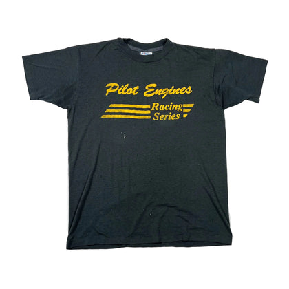 A dark charcoal gray short-sleeve t-shirt with a yellow graphic print on the front reading 'Pilot Engines Racing Series' with three yellow stripes, laid flat on a white background.