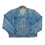 A light blue denim trucker jacket laid flat against a white background, featuring a classic collar, button-up front, and two chest pockets.