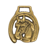 A vintage gold-toned metal horseshoe-shaped horsebit with an embossed horse head, shown on a white textured background.
