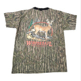 A short-sleeve camouflage t-shirt with a woodland tree-bark and leaf pattern, featuring a graphic of a white-tailed deer and the text 'WHITETAIL' on the front.