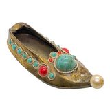 A vintage Tibetan-style metal shoe charm or pendant, decorated with turquoise, red coral, and a white pearl on a white textured background.