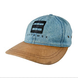 A baseball cap featuring a light blue denim crown with a black embroidered Antamex logo and text, paired with a curved brown leather brim, set against a plain white background.