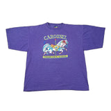 A purple heather short-sleeve t-shirt with a vintage carousel graphic on the front, laid flat on a white background. The graphic features a carousel horse and the text 'CAROUSEL' and 'PIMABOU SCHOOL OF ART'.