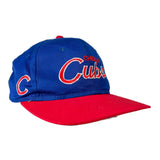 A Chicago Cubs baseball cap with a royal blue crown, red brim, and red and white embroidered lettering on a light gray background.
