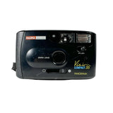 A black Halina Anscoo Vision Compact 35 Panorama film camera with a wrist strap, photographed on a light gray textured surface.