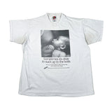 A white short-sleeve graphic t-shirt laid flat on a light gray background. The shirt features a black-and-white photo of a baby on the chest with the text 'Sometimes it's okay to suck up to the boss.