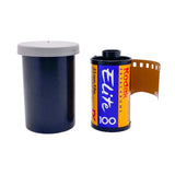 A roll of Kodak Elite 100 black and white film partially unspooled next to its dark blue plastic case with a gray lid, on a textured white background.
