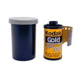 A vintage Kodak Gold Plus 100 35mm film canister next to its dark blue plastic roll case on a white textured background.