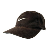 A dark brown Nike baseball cap with a white embroidered Swoosh logo on the front, set against a light gray studio background.