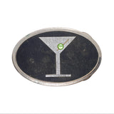An oval-shaped silver-toned belt buckle featuring a black enamel background with a silver martini glass design and a small green gemstone at the center, shown on a white textured background.