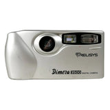 A silver Relisys Dimera 8500 digital camera with a textured metallic finish, featuring a prominent lens and flash unit on the front, set against a neutral light gray background.