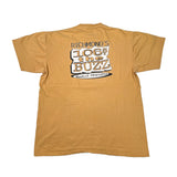 A tan short-sleeve t-shirt laid flat on a white surface, showing the back with a large graphic that reads 'RICHMOND'S 106.5 THE BUZZ New Rochelle Affirmation' in black and white.