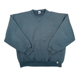A dark slate blue crewneck sweatshirt laid flat on a white background, featuring a small white and red tag on the bottom right hem.