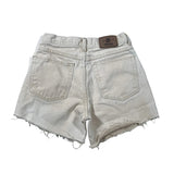 Back view of light beige denim shorts with a raw frayed hem, featuring two back pockets and a brown brand patch on the waistband.