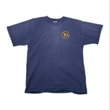 A navy blue short-sleeve t-shirt laid flat on a white fabric background, featuring a small circular yellow and white graphic printed on the lower left chest.