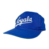 A royal blue baseball cap with 'The Royals' embroidered in white script on the front, photographed on a light gray studio background.