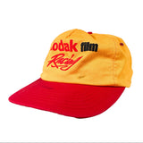 A vintage-style baseball cap with a yellow crown and a red curved brim, featuring 'Kodak film Racing' embroidered on the front.
