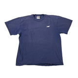 A faded blue short-sleeve t-shirt laid flat on a white fabric background, with a small white tag near the left sleeve and a black cap partially visible at the top edge.