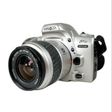 A Minolta Stadi MAXIMUM SLR camera in silver with a black and silver zoom lens, photographed on a clean white background.