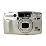 A silver Pentax IQZ 130M compact camera with a multi-lens system, photographed against a plain white background.