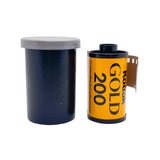 A vintage roll of Kodak Gold 200 film shown next to its dark blue plastic canister with a gray lid, on a white textured background.