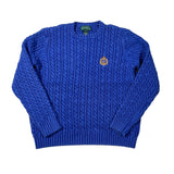 A royal blue cable-knit sweater with a small embroidered crest on the left chest, laid flat on a white background.