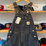 Blue denim overalls with a Carhartt logo on a hanger against a background of caps.